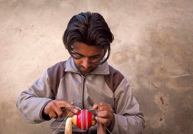 Photo (from the pamphlet, not a data chart): a worker hand-stitching a cricket ball.