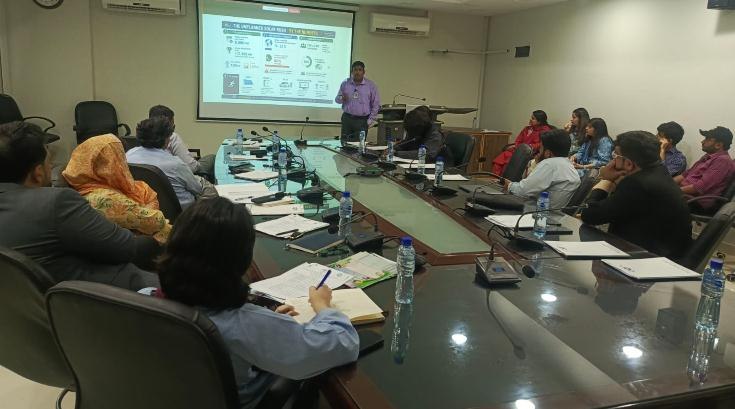 Photo from the report: a speaker presenting at the seminar, with a slide on Pakistan's compliance solar year.