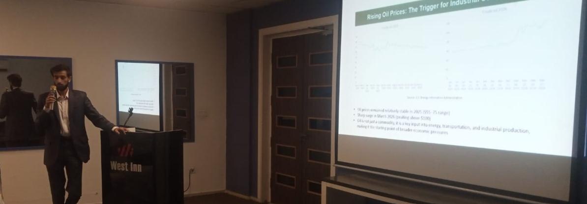 Photo from the report: a speaker presenting at the seminar, with a slide on rising oil prices as a trigger for industrial cost pressure.